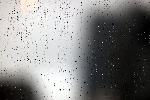 玻璃窗上佈滿雨滴，模糊了窗外的景色，象徵界線不清與情緒混濁的心理狀態。