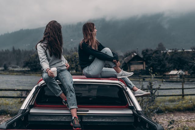 兩位年輕女性坐在車頂上遠望山景，象徵旅途中的友情與沉默陪伴的療癒力量。