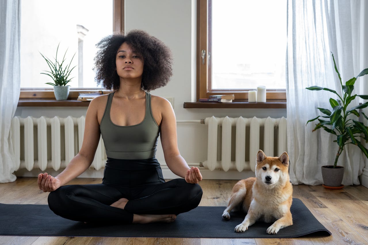 一位女性坐姿冥想，旁邊有隻柴犬靜靜陪伴，在家中木地板瑜珈墊上