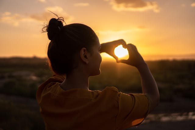 一位女性在夕陽下用雙手比出愛心，象徵著接納自我與內在平靜。