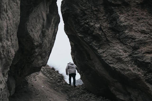 一位穿著外套的人正走在兩塊巨大岩石之間的山徑上，象徵從低谷中走出、踏上新方向的歷程。