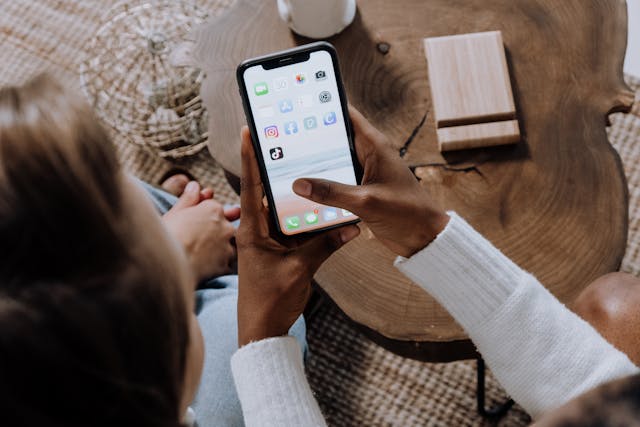 一位正在手持智慧型手機的人，手機螢幕上顯示 Instagram、TikTok 等社群媒體應用程式圖示。