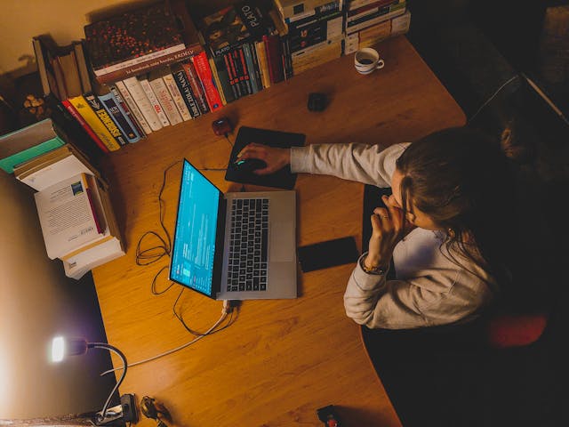 女性夜晚在書桌前加班工作，桌上擺滿書籍與電腦