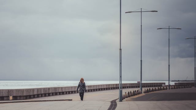 女子獨自走在海邊步道上，天空陰沉，走路成為一種安定心靈的力量，呼應《走路的人，河正宇》的閱讀心得