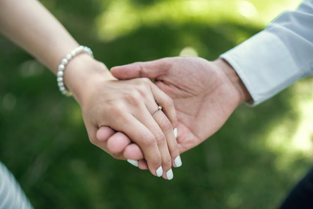 一對戀人牽著手,女子戴著訂婚戒指,陽光灑落在手心之間,象徵愛與承諾。