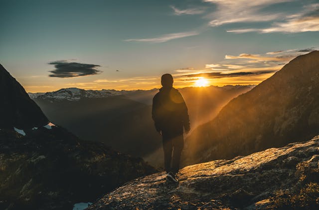 一名登山者站在山頂眺望夕陽，象徵在高峰時回望旅程並思考下一步。