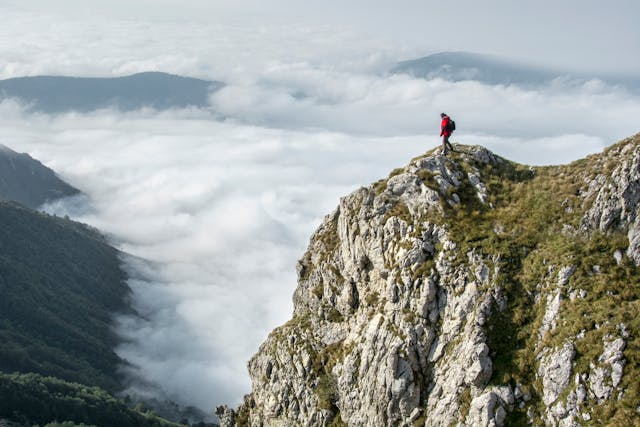 一名登山者站在山峰上俯瞰雲海，象徵攀登高峰與克服低谷的旅程。